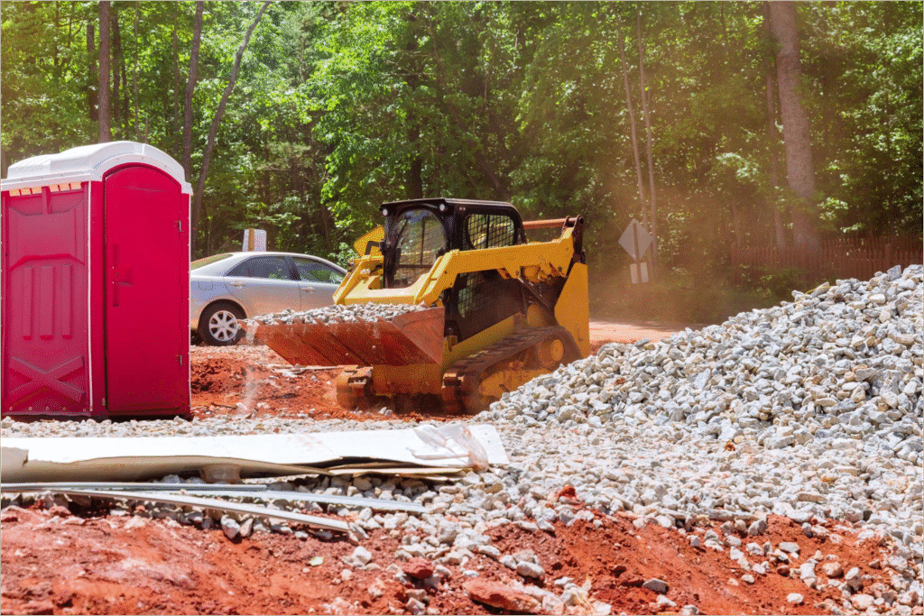 Construction site skid steer loader moving gravel, showing conditions where mobile oil change service trucks support field crews