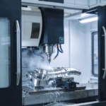 A professional technician monitors a modern 5-axis milling machine with CNC during precision machining of a titanium alloy aerospace component, with high-pressure coolant visible.